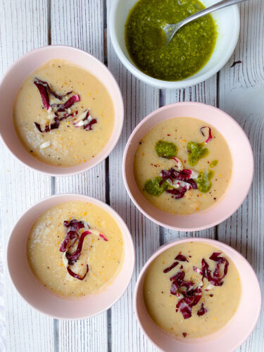 5 bowls, 4 of the bowls have white bean soup with a pinch of radicchio and pesto on top. The last bowl has pesto and a spoon inside it.