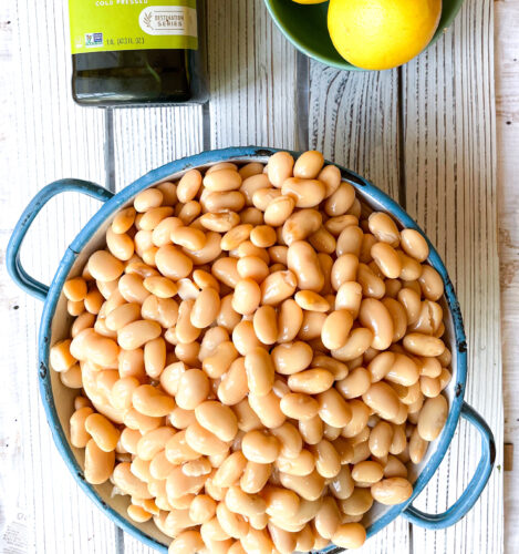 A bottle of olive oil, a bowl of lemons and a pot overflowing with butter beans.